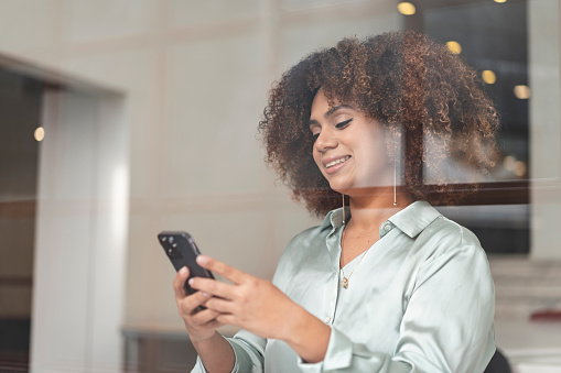 Smiling afro woman sending message on smartphone at workplace