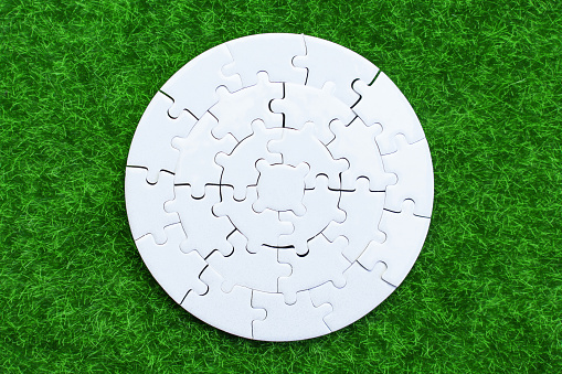Circular white puzzle resting on vibrant green grass. Unity, harmony and nature related concept.