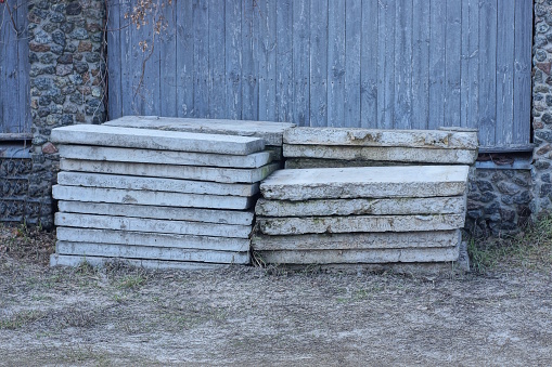 a pile of old gray square concrete slabs on the ground near a wall on the street