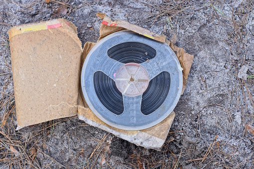 one old plastic magnetic reel for a tape recorder lies in a brown paper package on the gray ground on the street