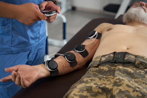 Doctor physiotherapist performs a physiotherapeutic procedure on a military man, the man has scars after being wounded