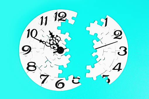 Close-up of a clock puzzle split in two uneven parts isolated on blue background. Creative time related concept.