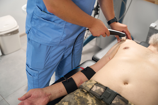 Military man with scars on his body at a hardware therapy session, the doctor uses a modern apparatus