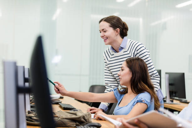 istock Young adult female tutor helps student in the computer lab 2063789640
