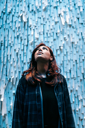 A high contrast profile portrait of a young African American woman with light skin tone looking up, standing in front of a wall of shredded paper.  Vertical with copy space.