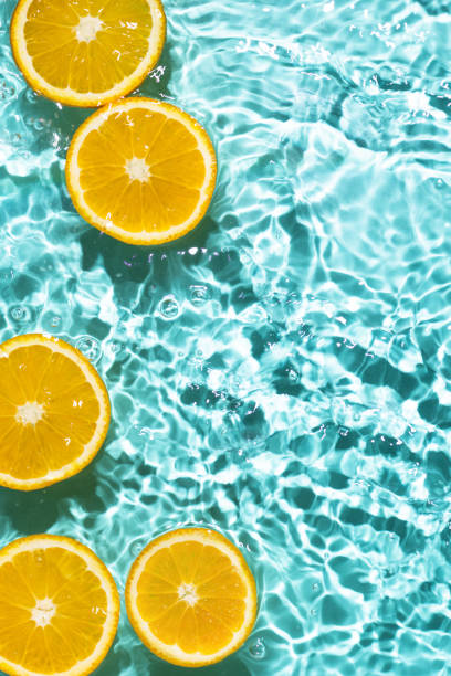 Creative summer background with orange fruit slices in swimming pool water.