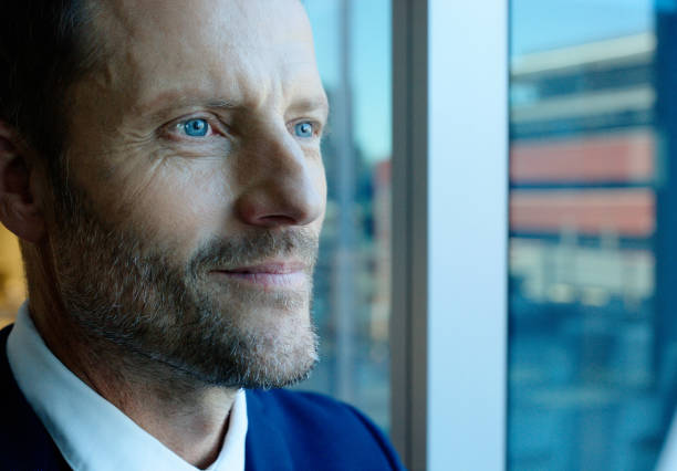 Thinking, office and business man by window with ideas, brainstorming project and planning. Corporate worker, professional and face of person for strategy, problem solving and solution in workplace