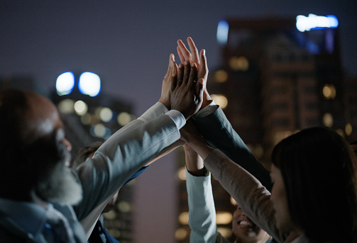 Business people, night and hands together in city with team for motivation, unity or outdoor collaboration. Group of employees touching for high five, success or late celebration in solidarity