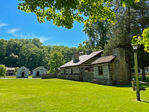 Mitchell, Indiana, USA - June 20, 2022:  Historic Apothecary, Mercantile and Lower Residence exterior in the recreated and restored 1800 Pioneer Village at Spring Mill State Park, near Mitchell, Indiana with beautiful blue sky and vivid green trees and grass copy space.