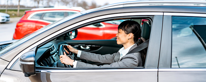 A mature Chinese businesswoman takes the wheel, her hands confidently steering the car through the city streets, a metaphor for her leadership journey, navigating her business towards success with determination and expertise