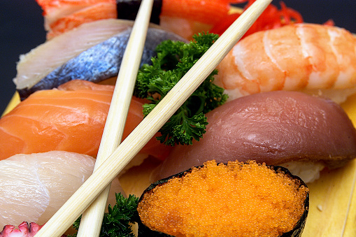 Assorted Japanese sushi rolls nigiri, sashimi, maki, salmon, tuna, served on wooden board on dark background