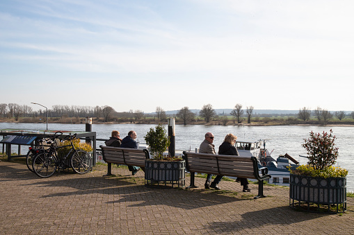 Tolkamer, Netherlands, March 3, 2024; People on a bench enjoy the view of the Rhine River.