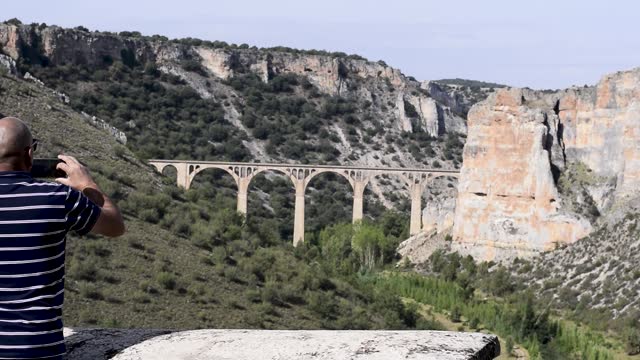 A man takes pictures of the landscape where an ancient aqueduct can be seen.