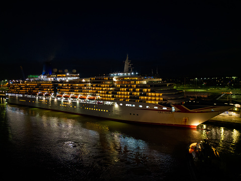 Arcadia cruise ship with Union Jack Flag at night with dark sky at Southampton Port, UK. Aerial view of a pilot boat with bright light towards bow of the cruise ship before departure. Lights reflection on the sea.