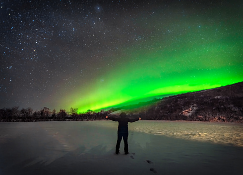 Aurora borealis and a man with arms rised in Iceland. Alone solo traveler. Sky with stars and polar lights. Night landscape with northern lights over the mountains