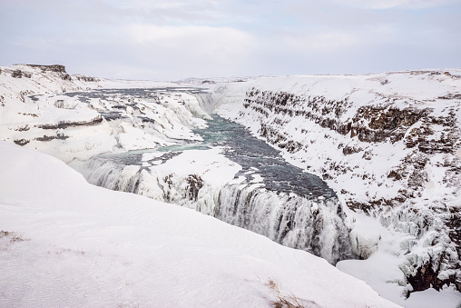 Gullfoss halffrozen waterfall in Iceland in winter daytime with clouds in the sk