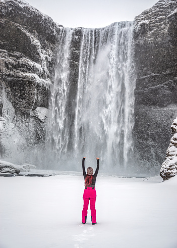 Iceland landscape photo of brave girl who proudly standing with his arms raised in front of water wall of Skogafoss waterfall.