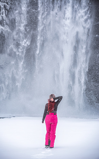 Skogafoss waterfall in Iceland. woman on her back with pink trousers, cap and hand on her head. Iceland