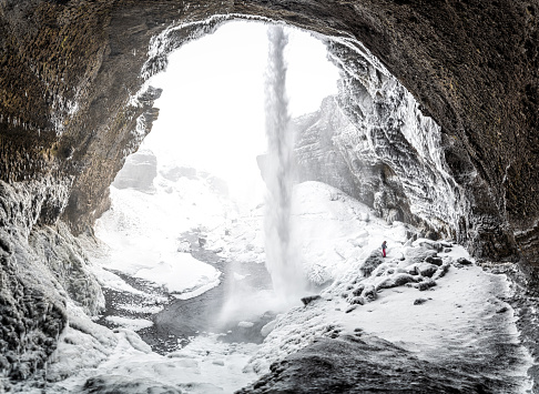woman hiker inside the Kvernufoss waterfall in Iceland in winter with everything snowed and frozen.
