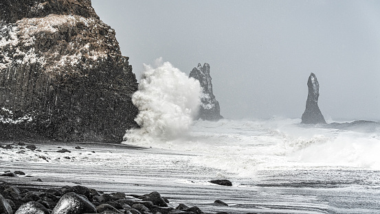 Extremely windy day at Reynisfjara black beach with big waves colliding to the rock formations in the Atlantic Ocean. View of Reynisdrangar rock formations on Reynisfjara Beach in a stormy windy day, Halsanefhellir, Iceland.