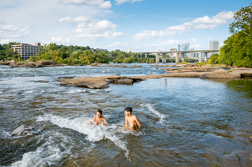 Two teenage friends swimming in the river rapids in summer