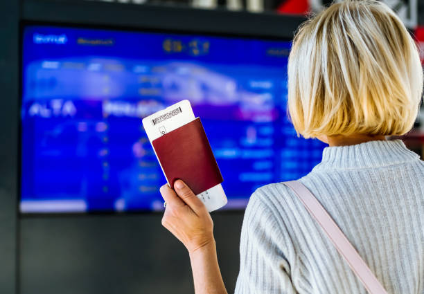 istock Woman holding passport in front of a flight information board 2064044549