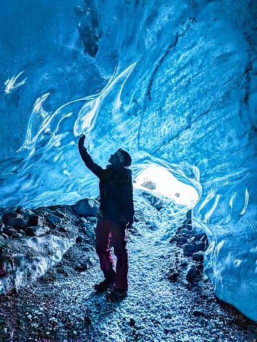 Woman standing at the entrance of the ice of an crystal blue ice cave at Vatnajokull glacier, Iceland