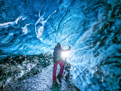 Woman standing at the bright opening of an ice cave in the Vatnajokull glacier in southeast Iceland