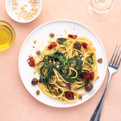 Spaghetti with Italian Agretti, Barba di frate or Saltwort or Salsola Soda, olives, anchovy, tomatoes, capers,  pine nuts and olive oil, spring Italian recipes. Pink soft background, square crop