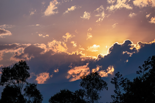 Beautiful afterglow over the eastern Andes mountains of central Colombia, with a pretty cloudy sky and some trees below.