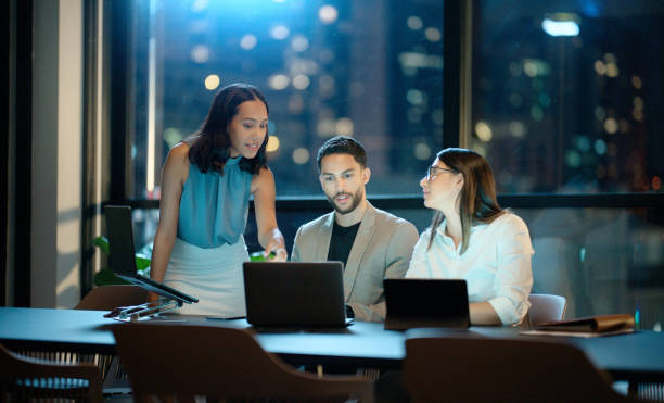 istock Night, talking or business people on laptop in discussion or conversation for education, support or advice. Teamwork, coaching or leader speaking of online info or research in a digital agency office 2064210366