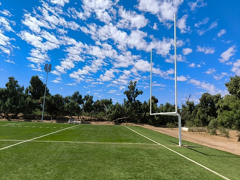 Soccer goalposts at Tempe Recreation Reserve, Sydney cast a shadow into the penalty area.  The shadow of a floodlight tower bisects the image.  Goalposts are required as essential equipment in playing a game of soccer, according to Law 1 of the FIFA Laws Of The Game.  This image faces east and was taken on a sunny afternoon in summer.