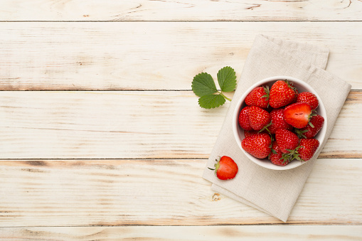 Strawberries in bowl on wooden background, top view
