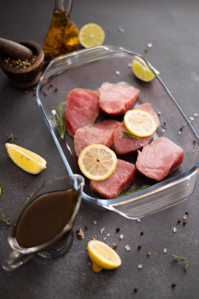 pieces of fresh tuna fish fillet in glass cooking dish and soy sauce marinade in a gravy boat - raw tuna steak marinated sauces stock-fotos und bilder