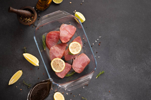 pieces of fresh tuna fish fillet in glass cooking dish and soy sauce marinade in a gravy boat - raw tuna steak marinated sauces stock-fotos und bilder