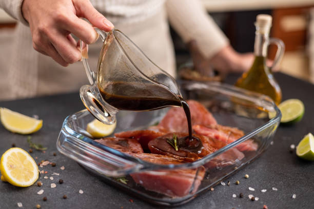 Woman pours soy sauce based marinade into glass cooking dish to marinate Pieces of Fresh tuna Fish fillet Woman pours soy sauce based marinade into glass cooking dish to marinate Pieces of Fresh tuna Fish fillet. marinade stock pictures, royalty-free photos & images