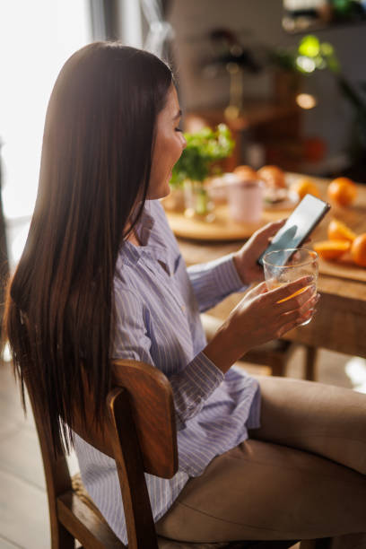istock Woman sitting at dining table, enjoying fresh orange juice and using smart phone 2064280965