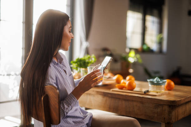 istock Woman sitting at dining table, enjoying fresh orange juice and using smart phone 2064280975