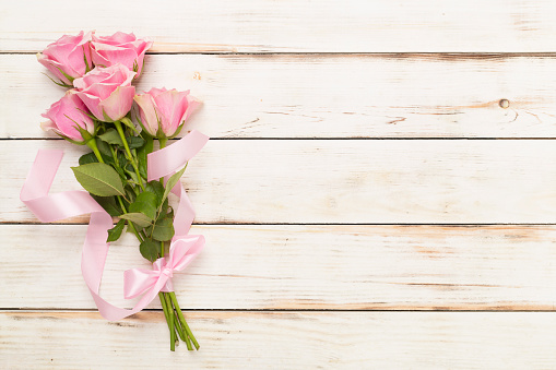 Pink roses with hearts on wooden background, top view.