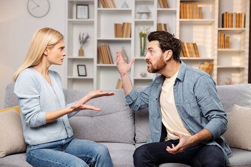 Emotional support for abused families depicted: An enraged husband raises his hand against his wife on their couch, poised to strike