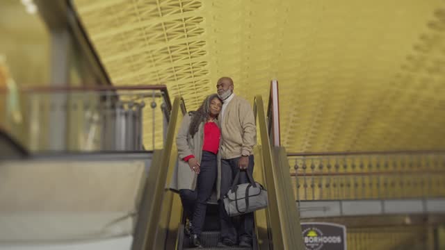 Affectionate senior couple coming down escalator in train station
