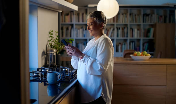 istock Phone, search and senior woman in a kitchen with social media, scroll or web communication. Smartphone, app or old person in a house streaming video, show or checking _ film selection at night 2064385419