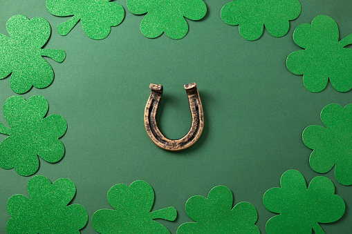 St. Patrick's day border with clover leaves and horseshoe on green background. View from above. Copy space. Festive greeting card.