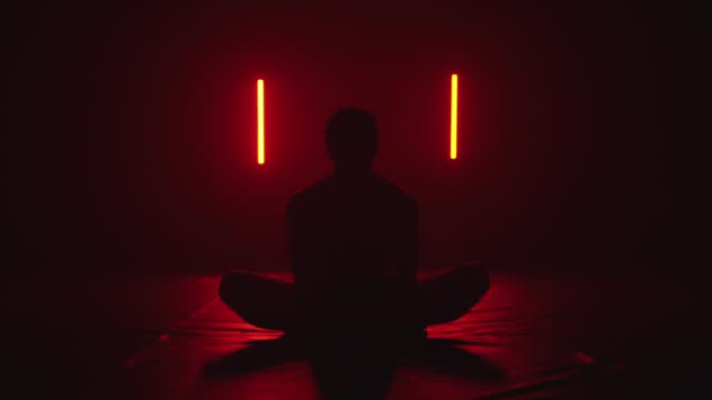 silhouette of a person stretching while sitting in lotus position in dark red room