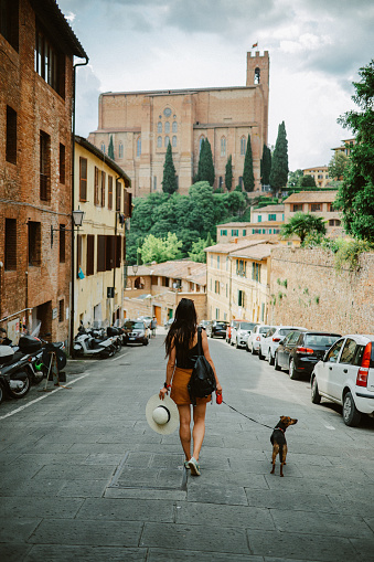 Female tourist traveling through Tuscany, visiting old town Siena, walking and sightseeing with her pet dog.
