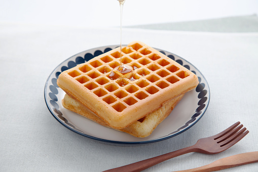 A stack of four Belgian waffles and three luscious red raspberries on a white plate with a melting slab of butter and maple syrup still barely trickling onto the butter. Isolated on white