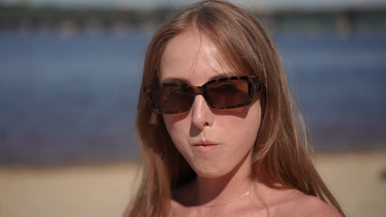 Close-up. A girl in sunglasses puts a cherry in her mouth and eats it. The girl looks at the camera smiling.