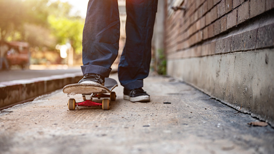 A close-up image of a male skater's feet riding on a skateboard on the street. Unrecognizable active skater legs practicing skateboarding on a city street.