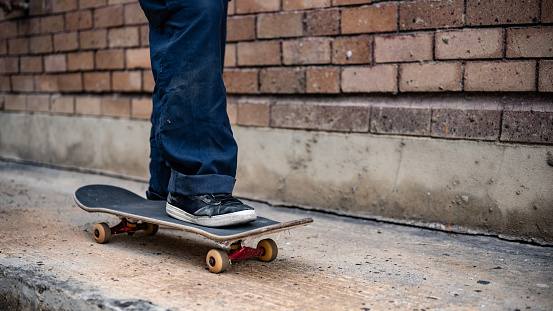 A close-up image of a male skater's feet riding on a skateboard on the street. Unrecognizable active skater legs practicing skateboarding on a city street.