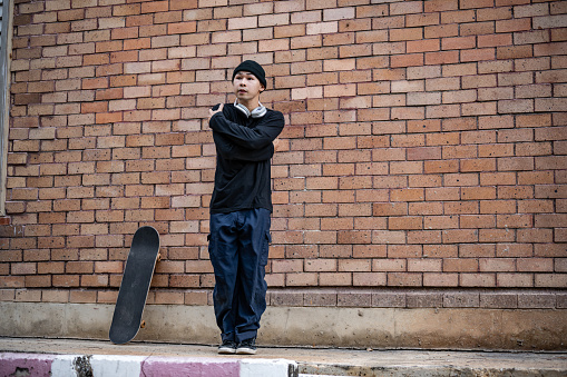 A cool, professional Asian male b-boy breakdancer in fashionable clothes is dancing on the footpath, performing his breakdance on the street outdoors.
